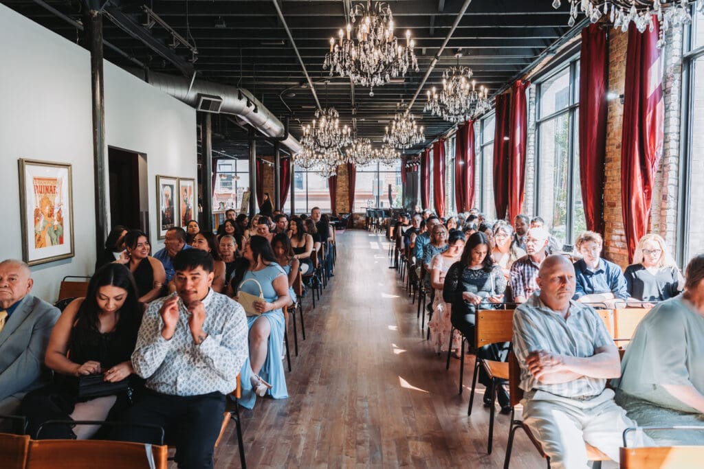 Wedding guests seated at Watson Block in Minneapolis beneath crystal chandeliers and red curtains — wedding venue photography by Eric Turner Photography, Minneapolis wedding photographer