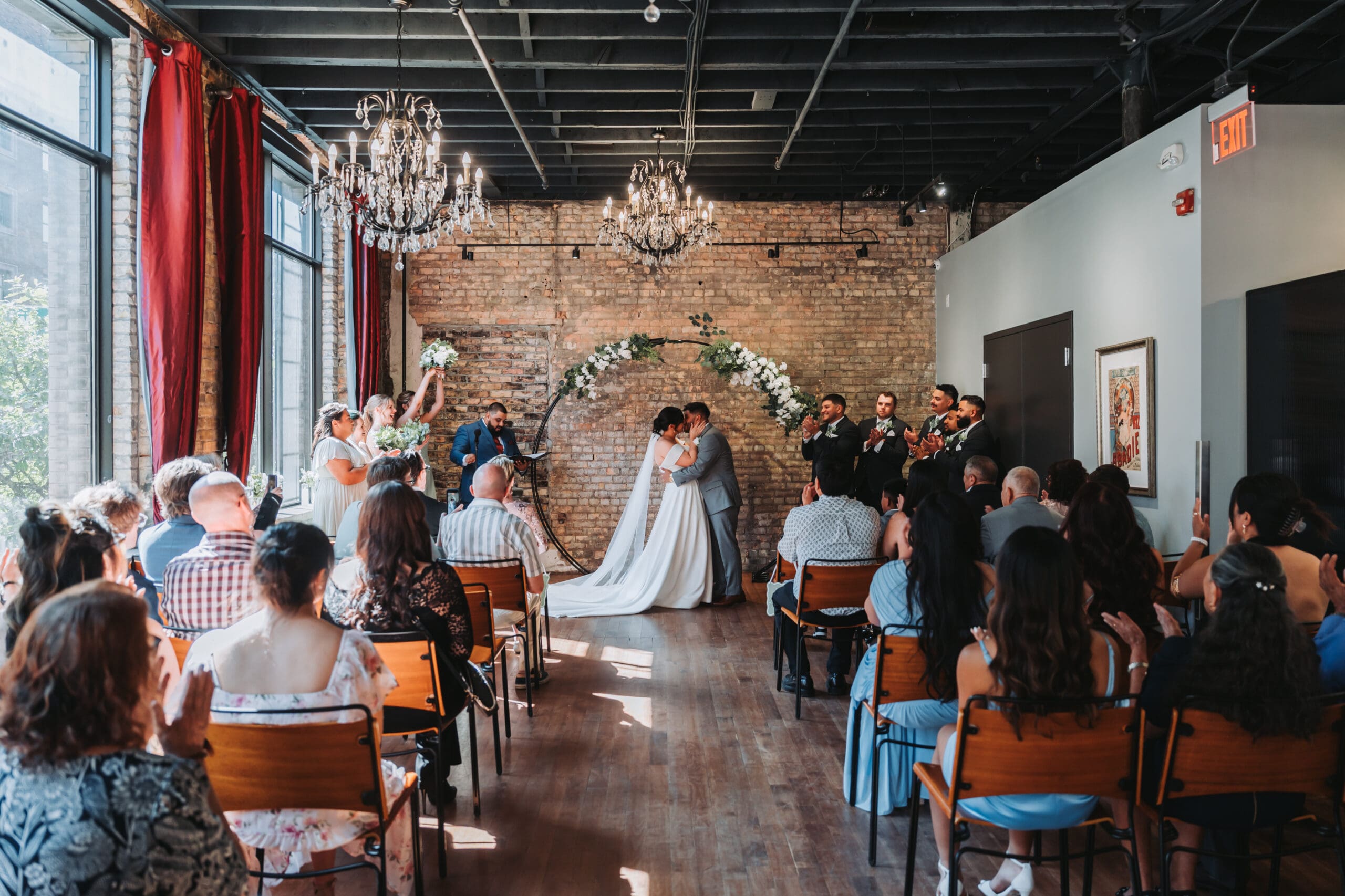 Bride and groom sharing their first kiss under a floral arch at Watson Block in Minneapolis, surrounded by exposed brick and chandeliers — wedding photography by Eric Turner Photography, Minneapolis wedding photographer